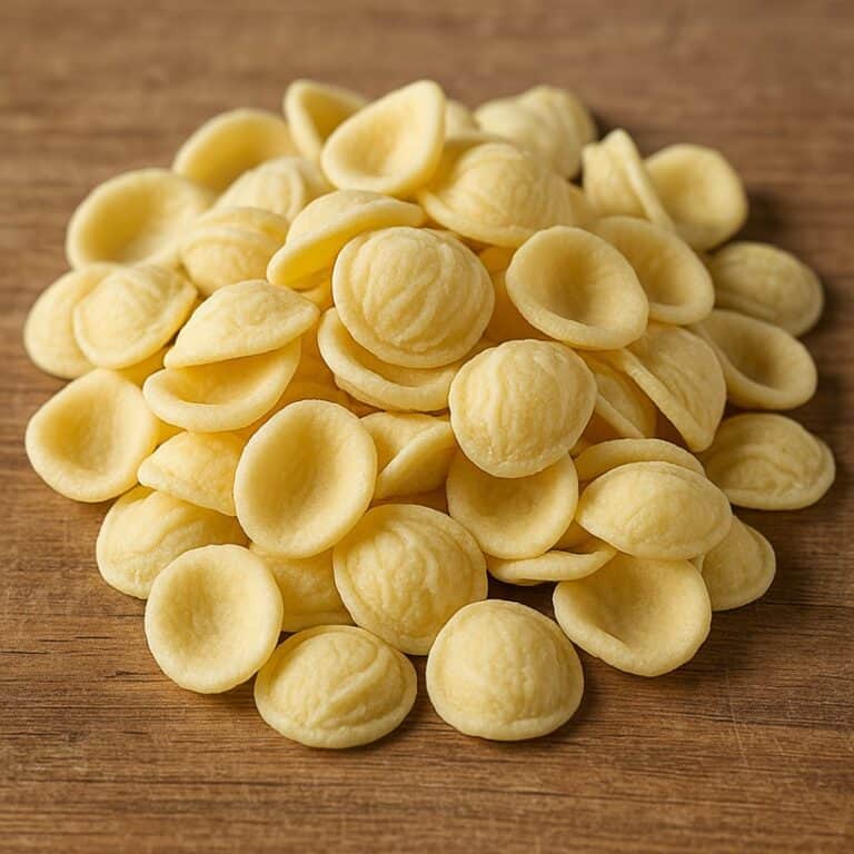 Un primo piano di orecchiette fresche disposte su un tagliere rustico di legno, pronte per essere cucinate.