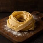 Nido di pappardelle fresche fatte a mano su tagliere di legno rustico