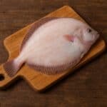 Platessa intera cruda su tagliere di legno con sfondo rustico