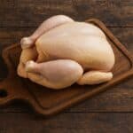 Pollo intero crudo con pelle giallo chiaro su tagliere in legno scuro