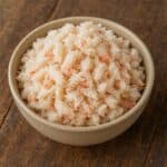 Polpa di granchio bianca con venature rosa in ciotola beige su tagliere di legno