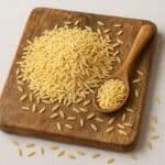 Risoni crudi disposti su tagliere in legno con cucchiaio colmo