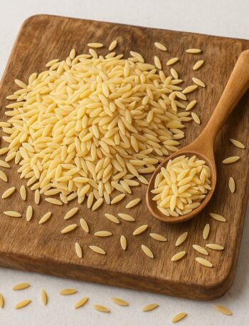 Risoni crudi disposti su tagliere in legno con cucchiaio colmo