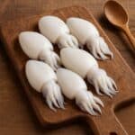 Seppioline bianche lucide su tagliere in legno con tentacoli