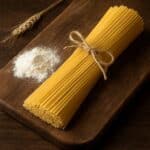 Mazzetto di spaghetti crudi legato con spago su tagliere in legno con farina e spiga di grano