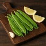 Taccole verdi su tagliere di legno con limone e uno spicchio d’aglio