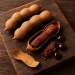 Baccelli di tamarindo aperti su tagliere in legno con polpa marrone e semi lucidi