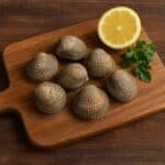 Tartufi di mare freschi su tagliere in legno, con mezzo limone e ciuffo di prezzemolo