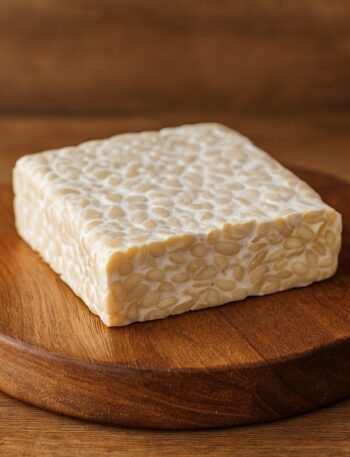 Panetto di tempeh su tagliere rotondo in legno con sfondo rustico