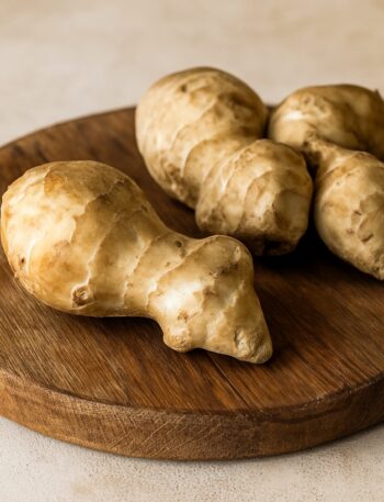Gruppo di tuberi di topinambur su tagliere rotondo in legno