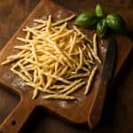 Trofie crude su tagliere rustico di legno con foglie di basilico fresco e coltello