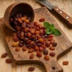 Uvetta dorata e scura su tagliere rustico con ciotola rovesciata, coltello e foglia di menta