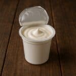 Vasetto bianco di yogurt con pellicola aperta su tavolo in legno