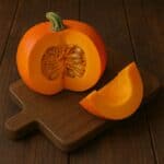 Zucca arancione tagliata a metà con fetta su tagliere di legno