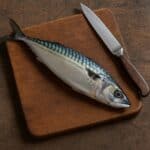 Sgombro intero con pelle argentata su tagliere in legno scuro