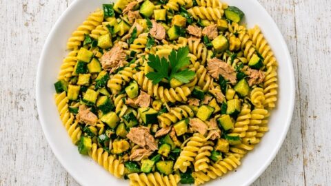 Piatto di pasta fredda con zucchine e tonno servito in piatto bianco su piano rustico, ricetta estiva facile e veloce.
