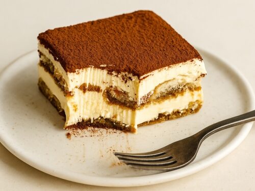 Fetta di tiramisù con strati visibili di crema e savoiardi, servita su piatto chiaro con forchetta