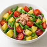 Insalata di patate estiva con fagiolini, pomodorini, cipolla rossa, tonno e basilico in ciotola bianca