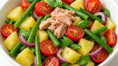 Insalata di patate estiva con fagiolini, pomodorini, cipolla rossa, tonno e basilico in ciotola bianca