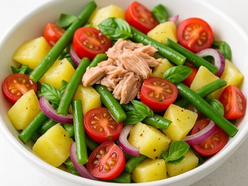 Insalata di patate estiva con fagiolini, pomodorini, cipolla rossa, tonno e basilico in ciotola bianca