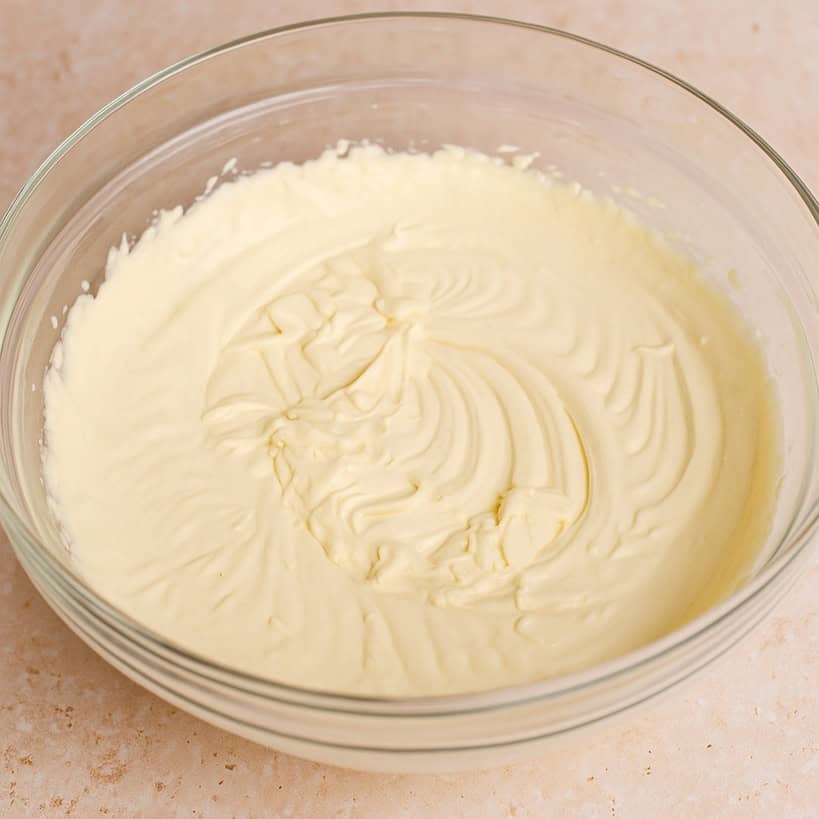 Crema al mascarpone liscia e omogenea in una ciotola di vetro su piano chiaro