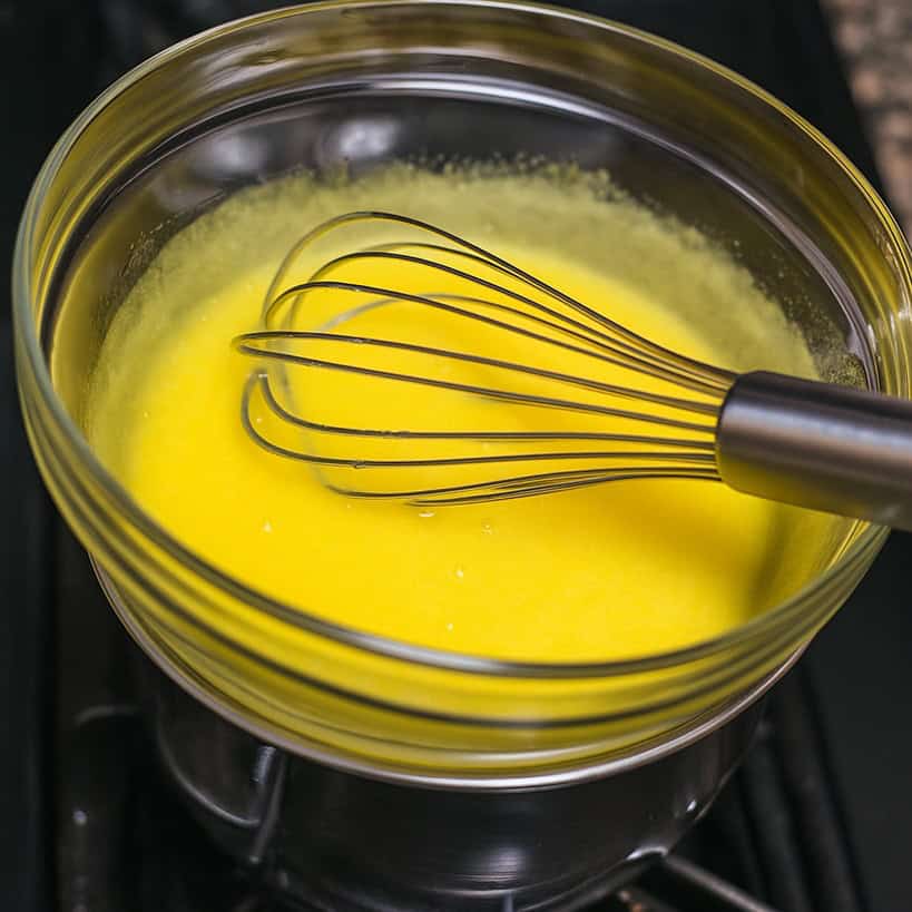 Ciotola di vetro con tuorli e zucchero montati a bagnomaria con frusta manuale