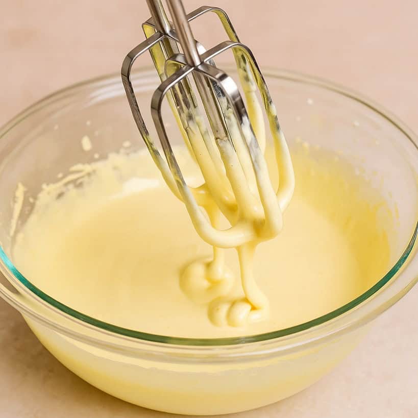 Tuorli e zucchero montati con fruste elettriche in una ciotola trasparente