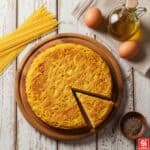 Una frittata di pasta con spaghetti dorata e croccante su un tagliere di legno, con uova, olio d'oliva e pepe in una cucina rustica.