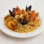 Risotto alla pescatora servito su un piatto bianco, con cozze, calamari, gamberi e vongole, guarnito con prezzemolo fresco.