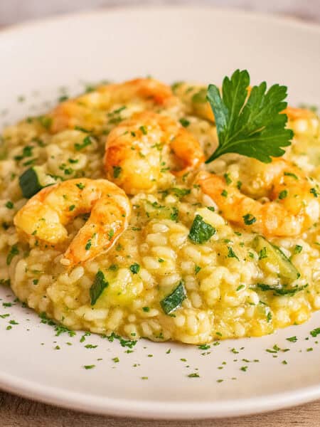 Risotto con zucchine e gamberetti cremoso servito in piatto bianco, decorato con prezzemolo fresco.