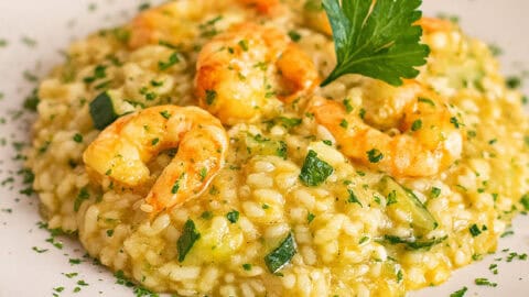 Risotto con zucchine e gamberetti cremoso servito in piatto bianco, decorato con prezzemolo fresco.