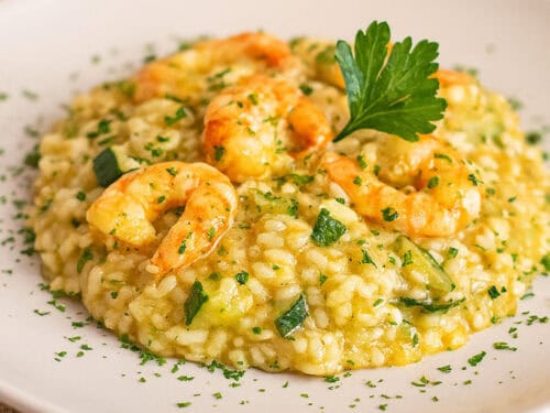 Risotto con zucchine e gamberetti cremoso servito in piatto bianco, decorato con prezzemolo fresco.