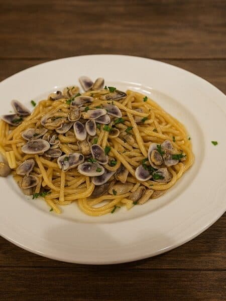Spaghetti con telline serviti su piatto bianco moderno