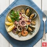 Insalata di mare con polpo, gamberi, calamari, cozze e vongole servita con limone.