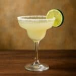 Margarita cocktail in bicchiere classico con bordo di sale e fetta di lime, su sfondo scuro.