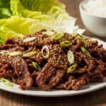 Piatto di Bulgogi con manzo marinato, grigliato e guarnito con semi di sesamo e cipollotto, servito con riso e lattuga.