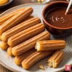 Un piatto di churros dorati e zuccherati, con uno spezzato che mostra l'interno soffice, accanto a una tazza di densa cioccolata calda.