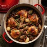 Coq au Vin in una cocotte, che mostra il pollo tenero, i funghi e le cipolline immersi nella salsa di vino rosso.