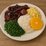 Feijoada brasiliana servita con riso bianco, cavolo riccio saltato e farofa, disposta su un piatto bianco con sfondo rustico