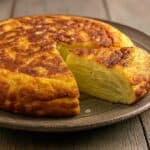 Un'autentica tortilla de patatas fatta in casa, con una fetta tagliata che ne rivela l'interno soffice e cremoso.