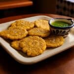 Piatto di Tostones cubani, platani verdi fritti due volte, dorati e croccanti, con una spolverata di sale e accompagnati da una ciotola di salsa mojo.