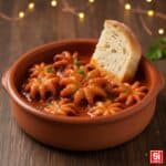 Primo piano del piatto di Polipetti Affogati al sugo denso, teneri, serviti in un coccio di terracotta con fetta di pane immersa per la scarpetta.