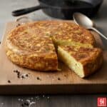 Primo piano di una Frittata di Patate alta e soffice, con superficie piatta e dorata, che mostra l'interno umido e le patate ben cotte. Ottima per merenda o cena.