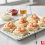 Tartine con gamberetti e salsa cocktail, preparate con pane in cassetta e gamberetti interi. Decorate con zeste di limone e erba cipollina tritata su un elegante piatto da portata bianco.