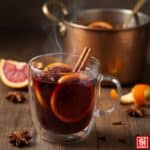 Vin Brulé caldo e fumante in tazza di vetro con cannella, anice stellato e fette d'arancia, ricetta originale.