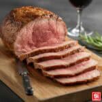 Arrosto di vitello cotto a puntino, tagliato a fettine molto sottili e succose su un tagliere di legno, guarnito con rosmarino fresco.