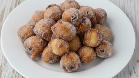 Fritole veneziane dorate e zuccherate su piatto bianco, con uvetta e decorazioni carnevalesche