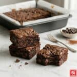Brownies al cioccolato fudgy impilati con crosticina lucida e teglia sullo sfondo