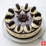 Oreo cheesecake senza cottura intera con ganache lucida e decorazione di panna e biscotti