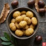 Castagne bollite sbucciate in una ciotola, viste dall’alto, con castagne intere e foglie di alloro